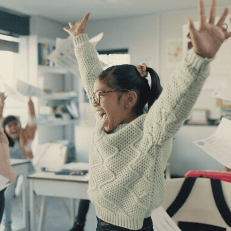 Children in a classroom throwing worksheets in the air, cheering.